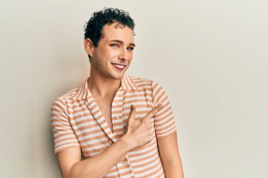 Makyaj yapan yakışıklı, rahat tişörtler giyen, gülümseyen, elleri ve parmaklarıyla yüzünü gösteren mutlu ve doğal bir ifade takınan bir adam. 