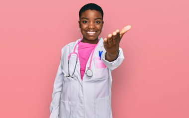 Genç Afro-Amerikan kadın doktor üniforması ve steteskop giyip dostça gülümseyerek selamlaşma ve selamlama sunuyor. başarılı iş. 