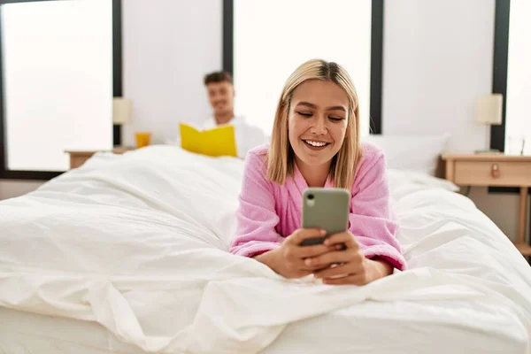 Joven Pareja Caucásica Leyendo Libro Usando Teléfono Inteligente Dormitorio —  Fotos de Stock