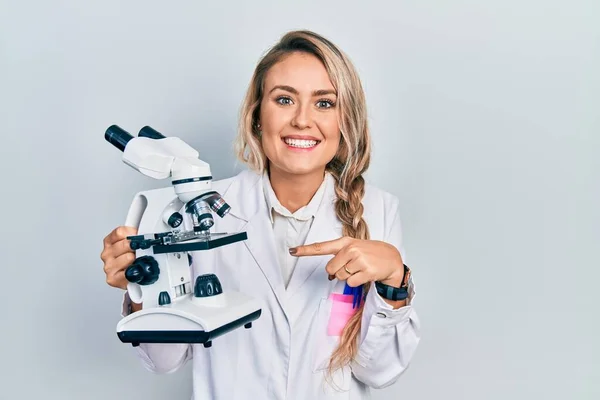 Hermosa Joven Rubia Sosteniendo Microscopio Sonriendo Feliz Señalando Con Mano —  Fotos de Stock