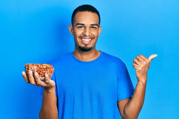 Joven Afroamericano Hombre Sosteniendo Tazón Cacahuetes Señalando Pulgar Hacia Lado — Foto de Stock