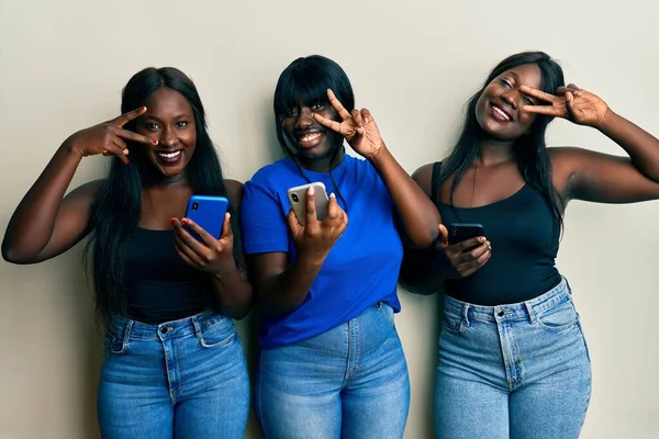 3人の若いアフリカ系アメリカ人の友人がスマートフォンで顔の上に指で平和の象徴をし 笑顔で勝利を示す — ストック写真