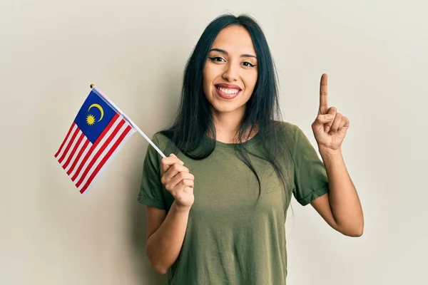 若いですヒスパニック系の女の子保持しているマレーシアのフラグ笑顔でアイデアや質問を指差す指で幸せな顔 ナンバーワン — ストック写真