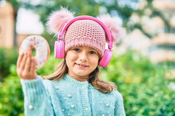 Αξιολάτρευτο Καυκάσιο Κορίτσι Που Χρησιμοποιεί Ακουστικά Και Τρώει Ντόνατ Στο — Φωτογραφία Αρχείου