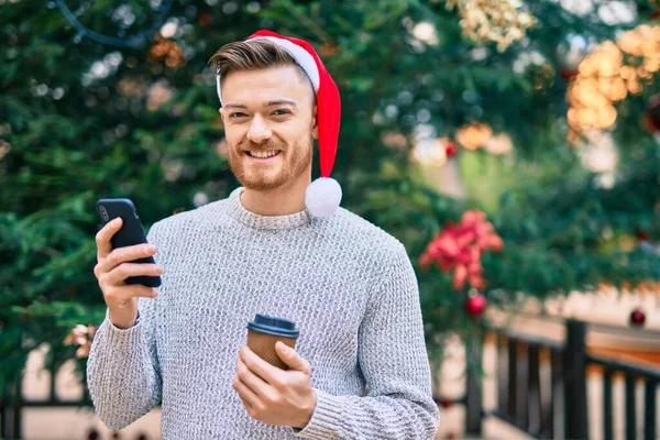 公園でスマホを使ってクリスマスの帽子をかぶった若い白人男性 — ストック写真