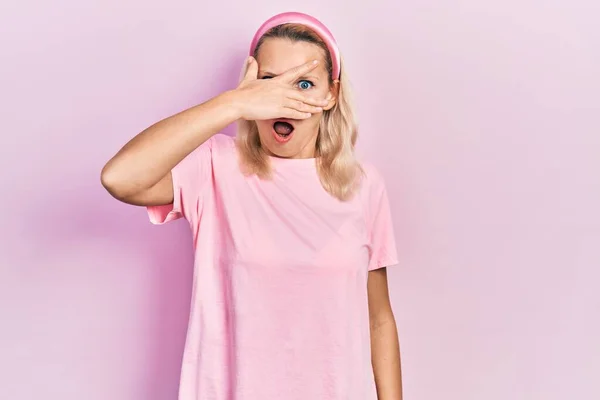 Hermosa Mujer Rubia Caucásica Vistiendo Casual Camiseta Rosa Asomándose Shock — Foto de Stock