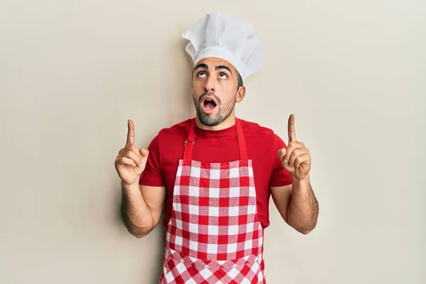 Junger Hispanischer Mann Bäckeruniform Staunt Und Überrascht Und Zeigt Mit — Stockfoto