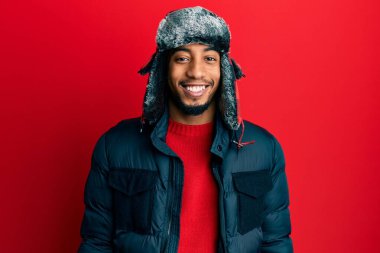 Sakallı, kışlık şapkalı ve ceketli, yüzünde mutlu ve havalı bir gülümseme olan Afrikalı genç bir Amerikalı. şanslı kişi. 