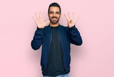 Gündelik kıyafetler giyen genç İspanyol adam dokuz numarayı gösterip işaret ederken kendinden emin ve mutlu bir şekilde gülümsüyor.. 