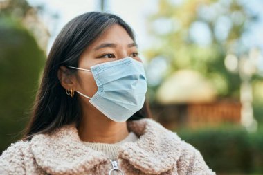 Şehirde duran, tıbbi maske takan genç Asyalı kadın..