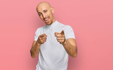 Dazlak, beyaz tişörtlü, sakallı, neşeli ve komik yüzlü bir adam kamerayı işaret ediyor. iyi enerji ve titreşimler. 