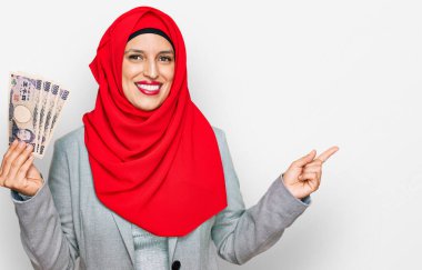 İslami tesettürlü güzel İspanyol kadın elinde Japon yen banknotları tutarken mutlu mesut gülümsüyor. 