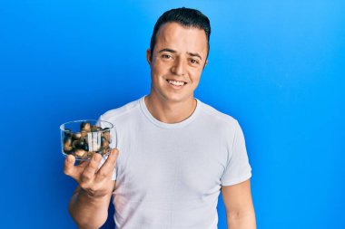 Elinde çiğ fındık tutan yakışıklı genç adam pozitif ve mutlu görünüyor ve kendine güvenen bir gülümsemeyle dişlerini gösteriyor. 