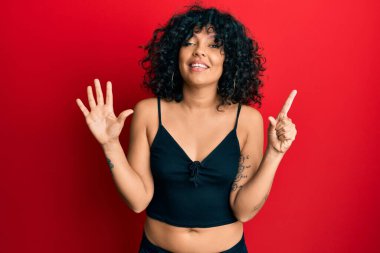 Kolsuz tişörtlü, sıradan giyinen genç İspanyol kadın altı numaralı parmaklarıyla gülümseyerek kendinden emin ve mutlu görünüyor.. 