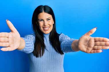 Güzel esmer kadın, gündelik giysiler içinde kameraya bakıp sarılmak için kollarını açmış gülümsüyor. Mutluluğu kucaklayan neşeli bir ifade.. 