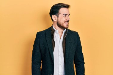 Sakallı, zarif bir iş ceketi giyen, yüzünde gülümseme, doğal bir ifade olan yakışıklı beyaz bir adam. Kendinden emin gülen. 