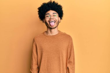 Afro saçlı, kışlık süveter giyen, neşeli bir ifadeyle dilini dışarı çıkaran Afro-Amerikalı genç bir adam. duygu kavramı. 