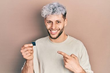 Modern boyalı saçlı genç İspanyol adam elinde SDxc kartı tutarak mutlu bir şekilde elini ve parmağını gösterdi. 
