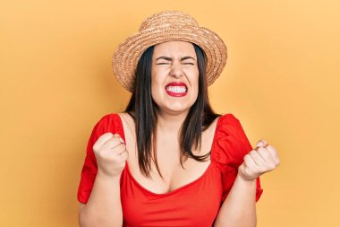 Genç İspanyol kadın yaz şapkası takıyor. Çok mutlu ve heyecanlı. Kolları havada, gülümseyen ve başarı için bağıran kazanan jestler yapıyor. kutlama konsepti. 