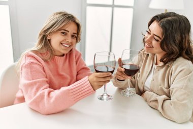 Genç çift mutlu bir şekilde kadeh kaldırıyor kırmızı şarap kadehiyle evde..