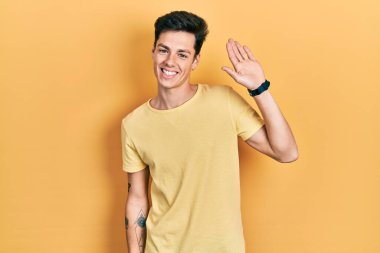 Sarı tişörtlü genç İspanyol adam merhaba diyor mutlu ve gülümsüyor, dostça bir hoş geldin jesti. 