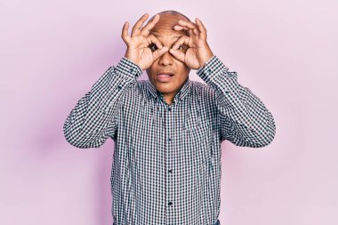 Orta yaşlı Latin bir adam sıradan kıyafetler giyiyor dürbün gibi jest yapıyor, gözleri parmaklarından bakıyor. çılgın ifade. 