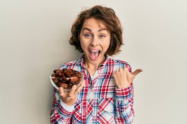 Genç esmer kadın elinde kaseyle başparmağını yana kaldırmış, ağzı açık gülümsüyor. 