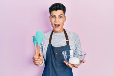 İspanyol asıllı genç adam ekmek hamuru ve yemek aletleri tutuyor şaşkınlık ve şaşkınlık içinde bir ifade, korku ve heyecan dolu bir yüz.. 