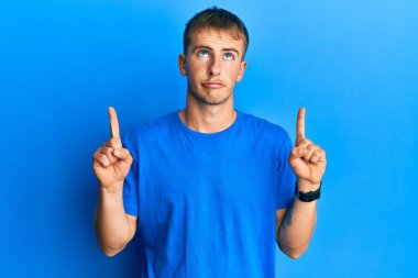 Gündelik mavi tişört giyen genç beyaz adam üzgün ve üzgün görünüyor, parmaklarıyla yönü gösteriyor, mutsuz ve depresif.. 