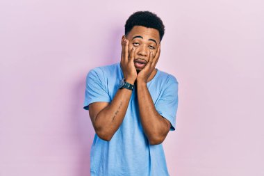 Genç Afro-Amerikalı adam, günlük mavi tişört giyiyor. Yorgun eller, yüzünü kapatıyor. Depresyon ve üzüntü. 