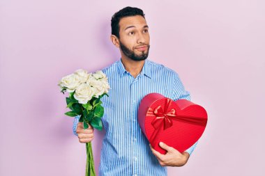 Sakallı İspanyol bir adam yıldönümü hediyesi tutuyor ve bir buket çiçek gülümsüyor.. 