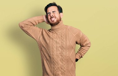 Gündelik kıyafetler giyen, boynu ağrıyan, eliyle boynuna dokunan, kas ağrısı çeken genç İspanyol bir adam. 