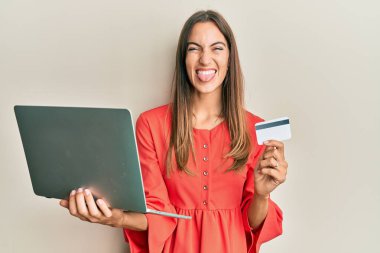 Genç, güzel bir kadın dizüstü bilgisayar ve kredi kartı tutuyor. Dilini komik bir ifadeyle dışarı çıkarıyor.. 