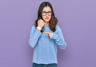 Gündelik kıyafet ve gözlük takan genç ve güzel bir kadın saati, sabırsızlığı ve rahat bir ifadeyle kameraya bakmayı işaret ediyor. 
