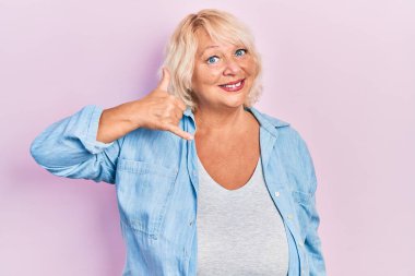 Orta yaşlı, sarışın, sıradan kıyafetler giyen, gülümseyen, el ve parmaklarıyla telefonla konuşan bir kadın. iletişim kavramları. 