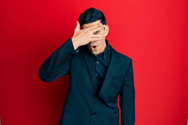 İş kıyafetleri giymiş yakışıklı İspanyol bir adam. Şoka girmiş, yüzünü ve gözlerini kapamış, utanmış bir ifadeyle parmaklarından bakıyor.. 