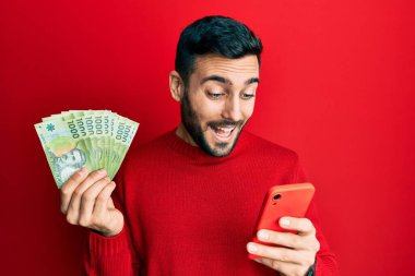 Genç İspanyol adam akıllı telefon kullanıyor elinde Şili pezosu banknotları sırıtıyor ve kahkahalarla gülüyor çünkü komik çılgın bir şaka.. 