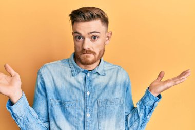 Genç, kızıl saçlı, sıradan bir kot gömlek giyen, kafası karışık, kolları açık, hiçbir fikri olmayan, şüpheli bir yüzü olan bir adam.. 