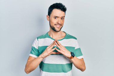 Latin asıllı genç adam rahat ve neşeli gülümseyerek ellerini birleştirip gülümsedi. Başarı ve iyimserlik 