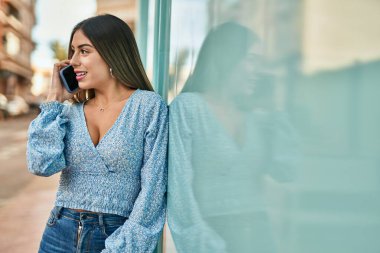 Genç İspanyol kadın gülümsüyor. Şehirdeki akıllı telefondan konuşuyor.
