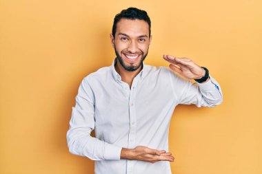 Sakallı, iş gömleği giyen, elleri ve büyük boy işareti gösteren İspanyol bir adam. Ölçü sembolü. Kameraya bakıp gülümsüyor. ölçüm kavramı. 