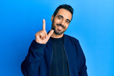 Bir fikir veya soruyla gülümseyen gündelik kıyafetler giyen genç İspanyol adam, bir numara, mutlu bir yüzle işaret ediyor. 