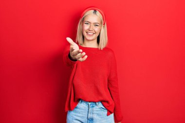 Hoş geldin ve hoş geldin demek için gülümseyerek el sıkışan kırmızı süveter giyen güzel sarışın kadın. başarılı iş. 