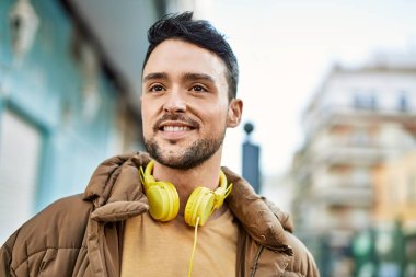 Şehirde kulaklık takarak mutlu gülümseyen genç İspanyol adam..