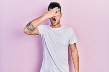 Günlük beyaz tişört giyen genç İspanyol adam şok içinde yüzünü ve gözlerini kapayarak parmaklarından korkuyla bakıyor. 