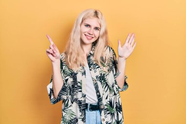 Sarı saçlı, güzel beyaz kadın tropikal gömlek giyiyor ve altı numaralı parmaklarıyla işaret ederken kendinden emin ve mutlu gülümsüyor.. 