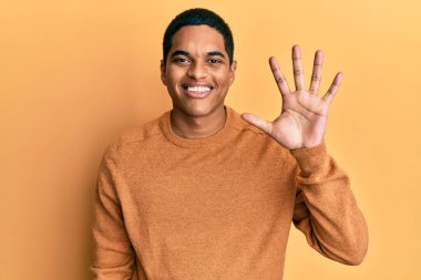 Genç, yakışıklı, sıradan bir süveter giyen, beş numaralı parmaklarını göstererek gülümseyen, kendinden emin ve mutlu bir İspanyol.. 