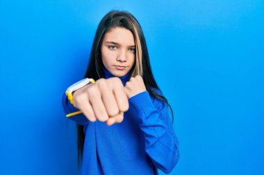 Balıkçı yaka kazak giyen genç esmer kız dövüşmek için yumruk sallıyor agresif ve öfkeli saldırı, tehdit ve şiddet. 