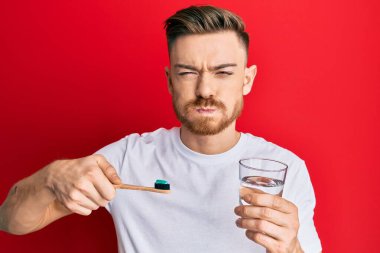 Kızıl saçlı genç adam diş fırçasıyla diş macunu ve bir bardak su şişiren komik yüzlü yanak tutuyor. Ağzı havayla şişer, havayı yakalar.. 