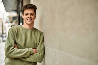 Genç İspanyol adam mutlu bir şekilde gülümsüyor şehirde çapraz hareketlerle.